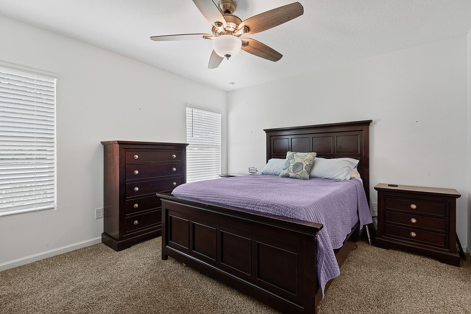 Spacious primary bedroom with dark-wood furnishings and plush carpet